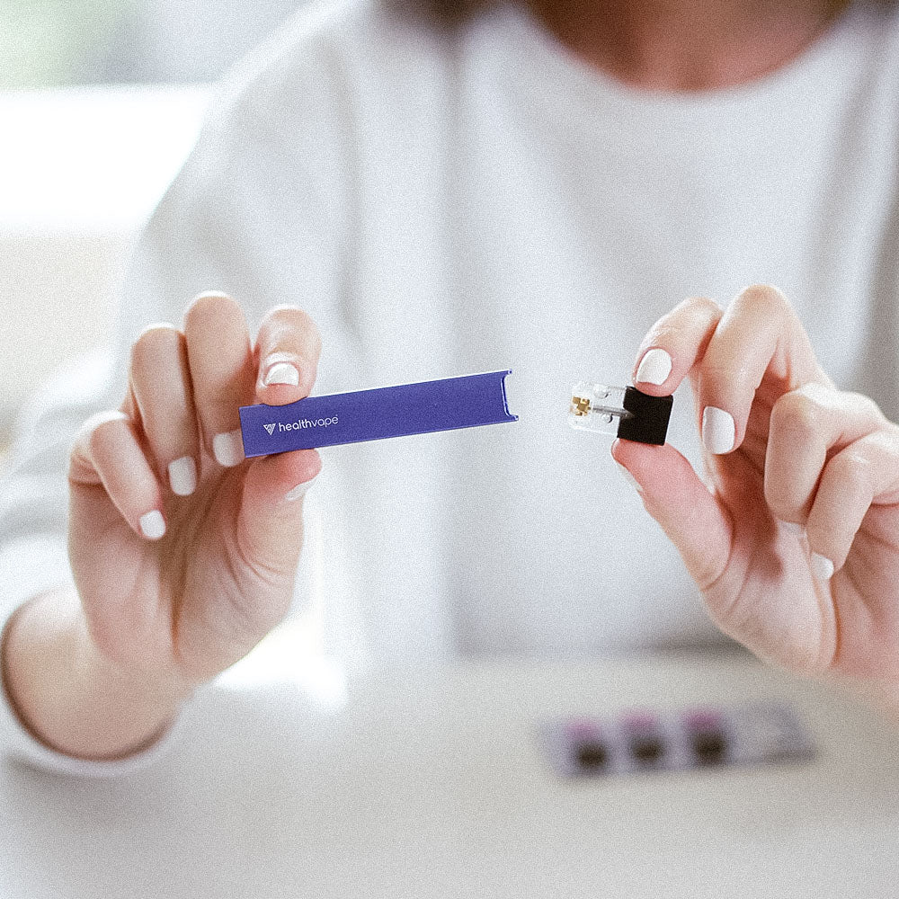 Person inserting a vape pod into a blue HealthVape battery device on a light background.