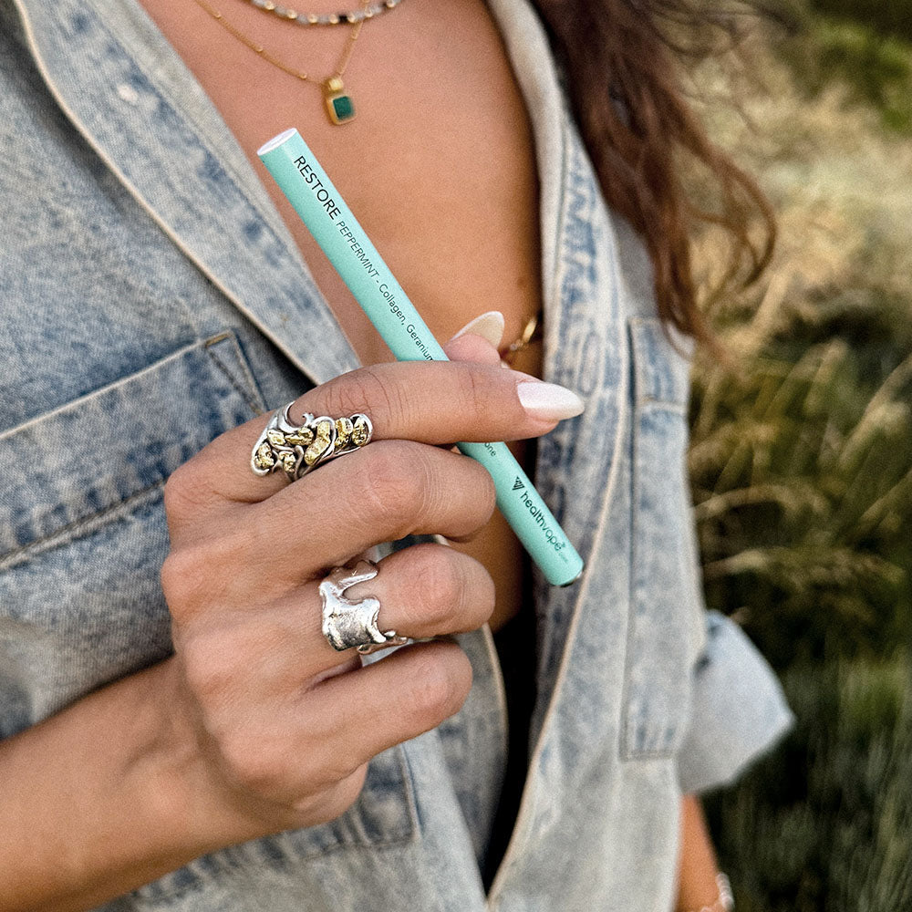 Person holding a teal HealthVape RESTORE disposable vape pen outdoors.
Image 3 (restore-lychee-03)