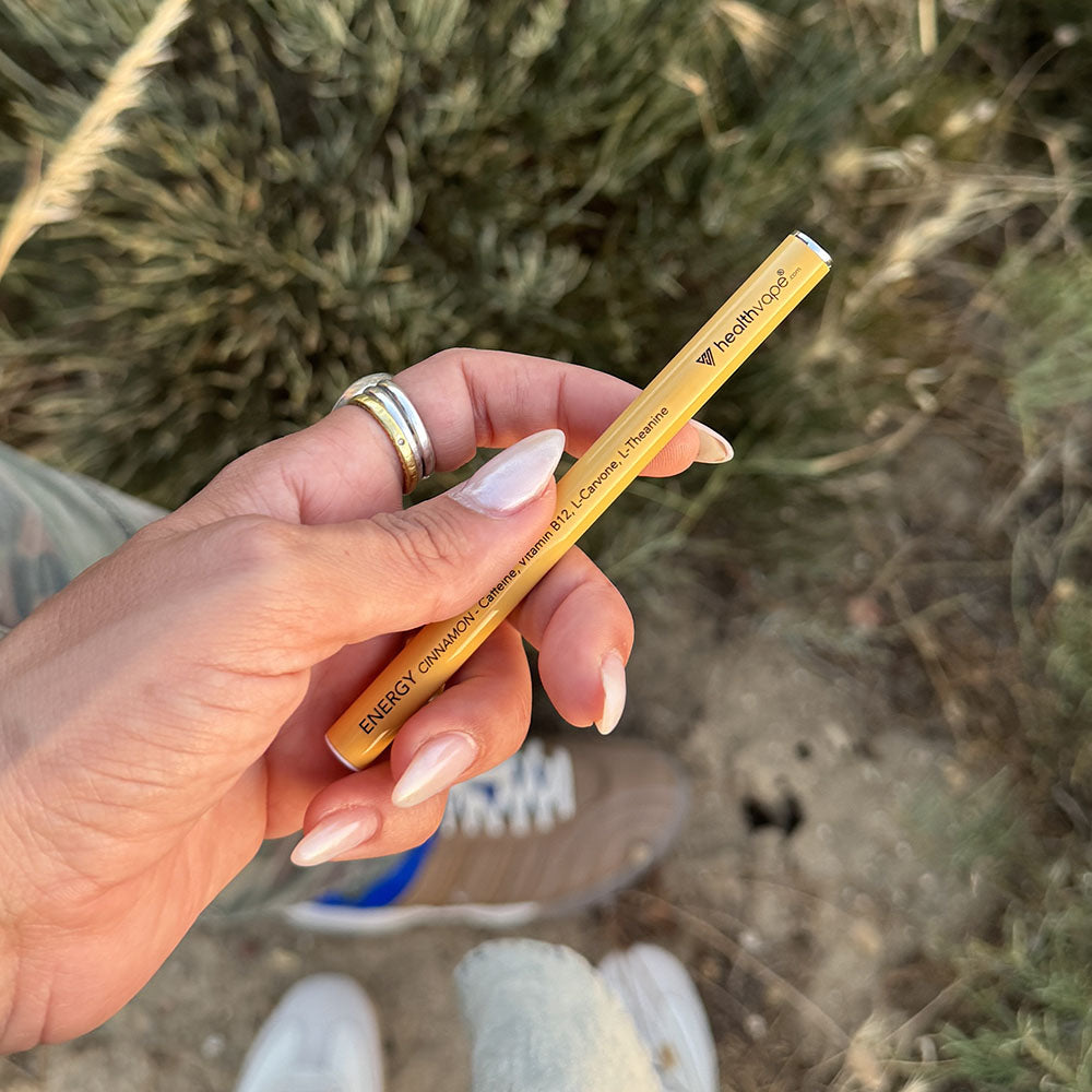 Hand holding a yellow HealthVape Energy vape pen outdoors with natural background