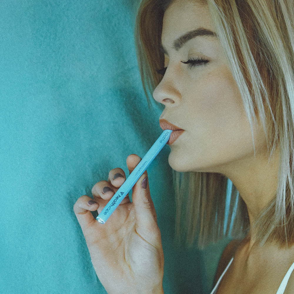 Woman holding lavender HealthVape Soothe pen against teal background